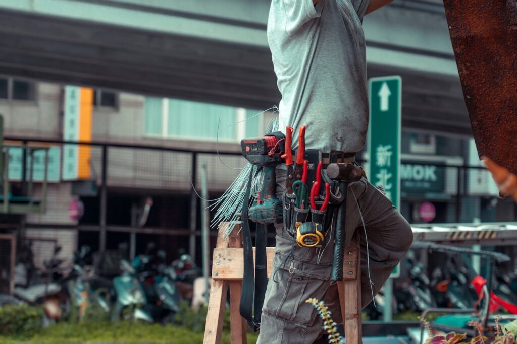 A Man Wearing Work Clothes and a Belt with Tools Standing on a Ladder